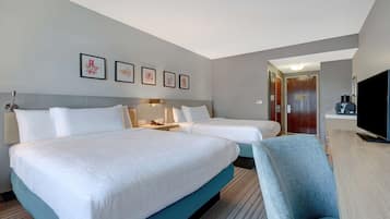 Habitación de hotel con dos camas, un escritorio, una silla, un televisor y cuadros en la pared.