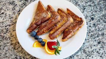 Un plato de tostadas francesas con arándanos, fresas y rodajas de naranja.