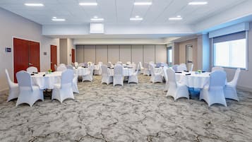 A conference room with multiple tables and chairs, carpeted floor, and a large window.