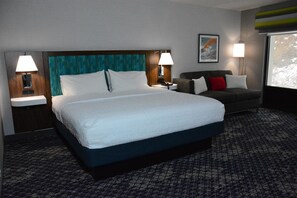 Habitación de hotel con una cama grande, lámparas de noche, un sofá y ventana con vistas.
