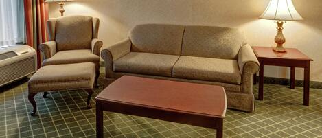 Ein Hotelzimmer mit einer Couch, einem Sessel und einem kleinen Tisch. Auf jeder Seite der Couch steht eine Lampe.
