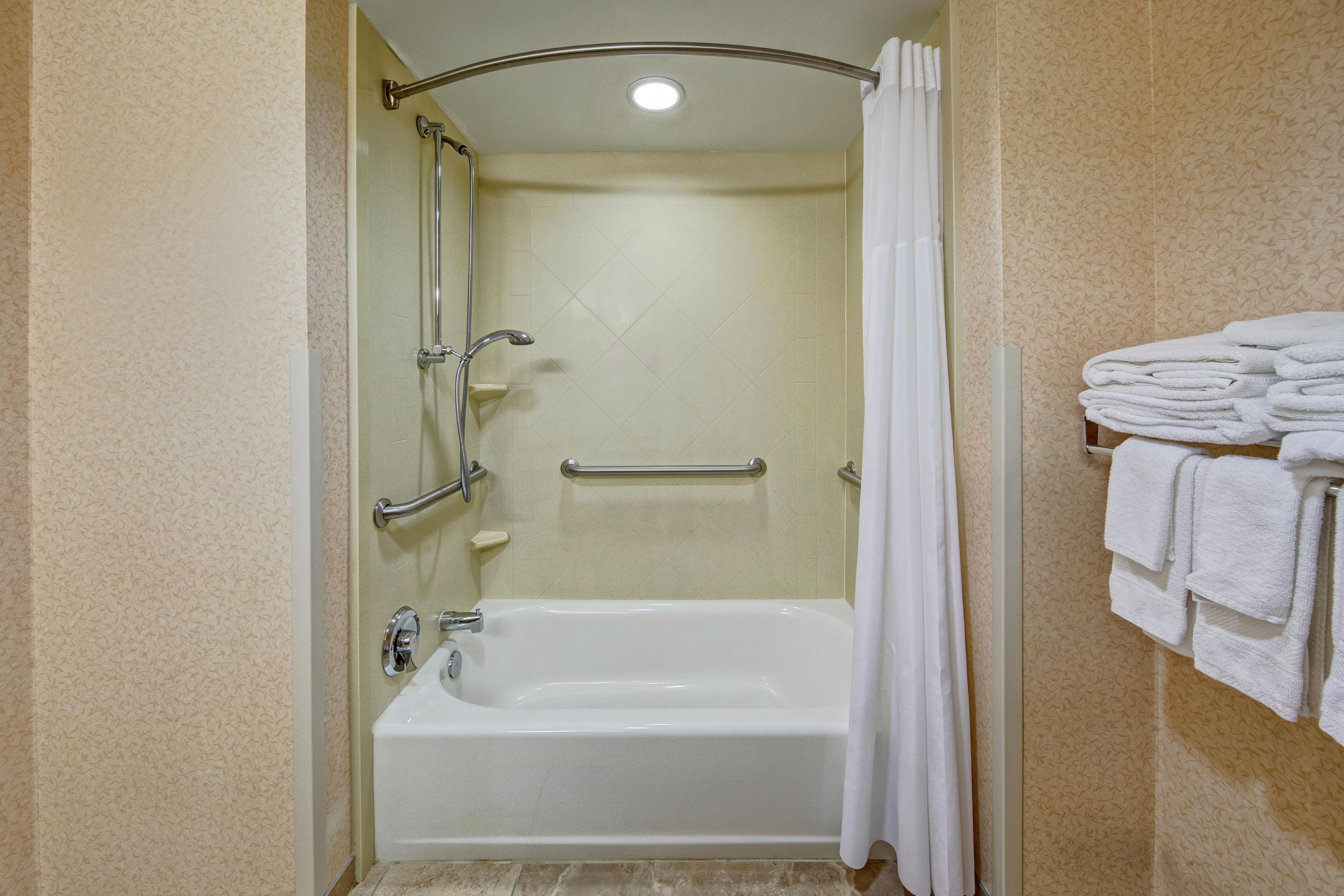 Ein Badezimmer mit Badewanne, Dusche und Handläufen.