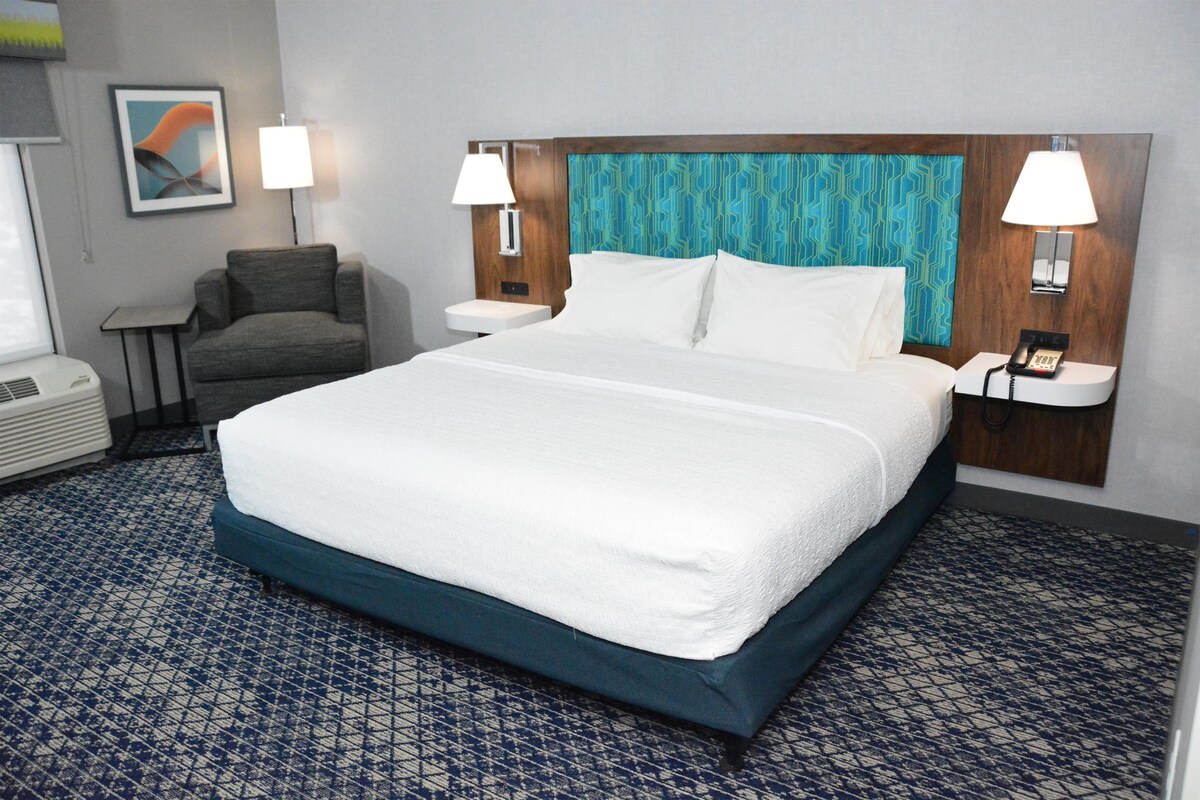 Habitación de hotel con una cama grande, dos lámparas de noche, una silla, una mesita y un teléfono en la pared.