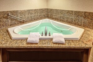 A corner bathroom with a freestanding bathtub, granite countertop, and a handrail.