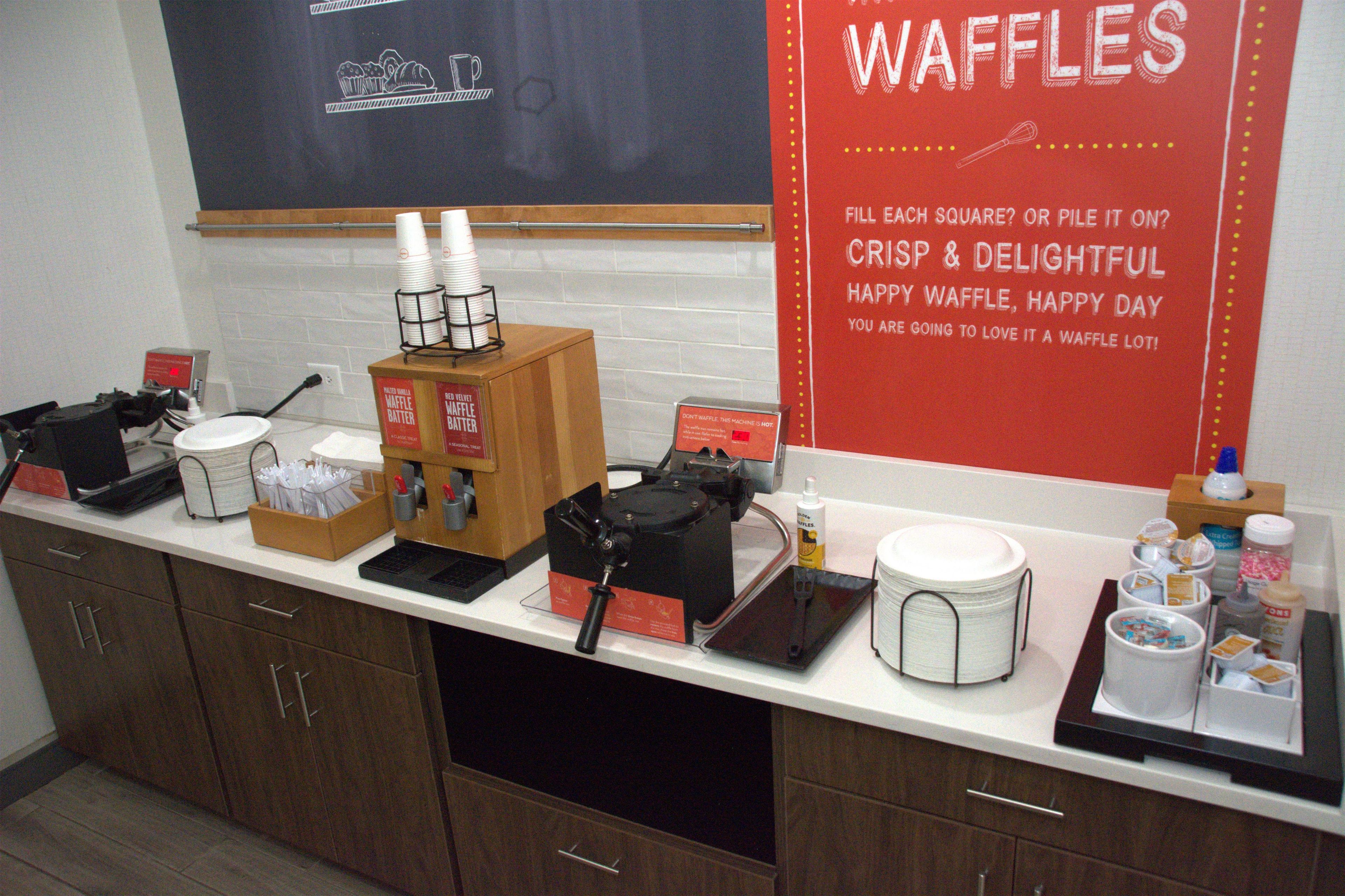 Una encimera de cocina con equipo para hacer gofres, cajas de masa para gofres y un cartel que promociona los gofres.