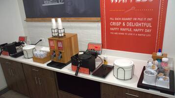 Una encimera de cocina con equipo para hacer gofres, cajas de masa para gofres y un cartel que promociona los gofres.