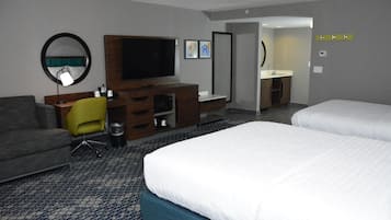 A hotel room with a bed, a desk with a TV, a chair, a mirror, and a bathroom.