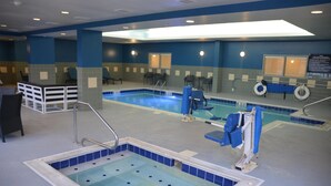 En indendørs swimmingpool med blå og hvide fliser, en redningsbøje og en badestige.