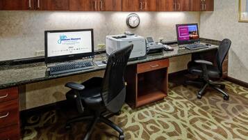 Oficina de hotel con dos escritorios, computadoras, sillas, un reloj y piso alfombrado.