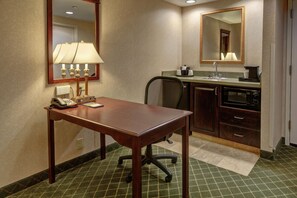 A hotel room with a wooden desk, a telephone, a lamp, a chair, a sink, a mirror, and a microwave. - Hampton Inn Cambridge (Cambridge)