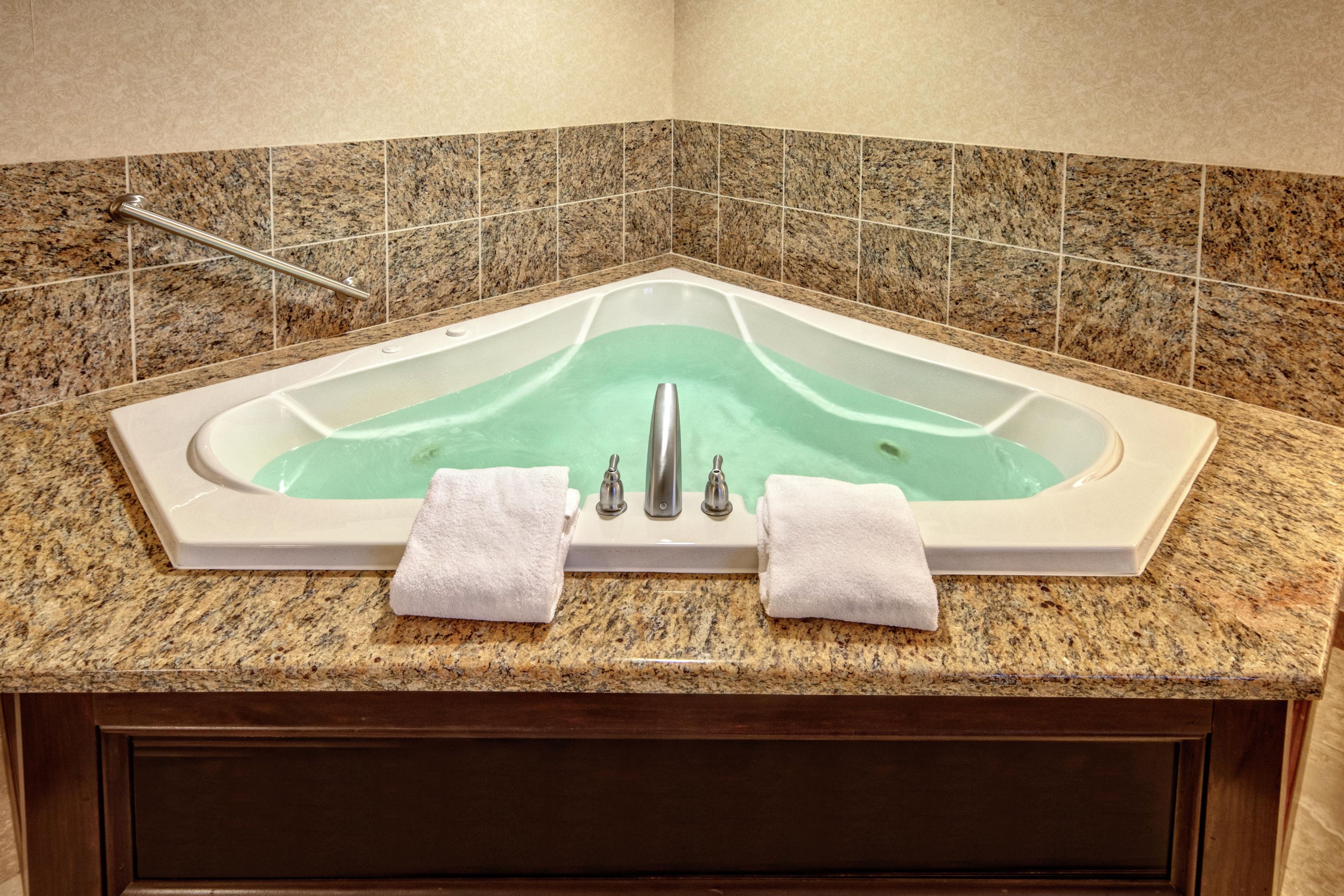 A corner bathroom with a freestanding bathtub, a handrail, and two towels on the countertop.