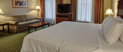 A hotel room with a large bed, a sofa, a television, and curtains.