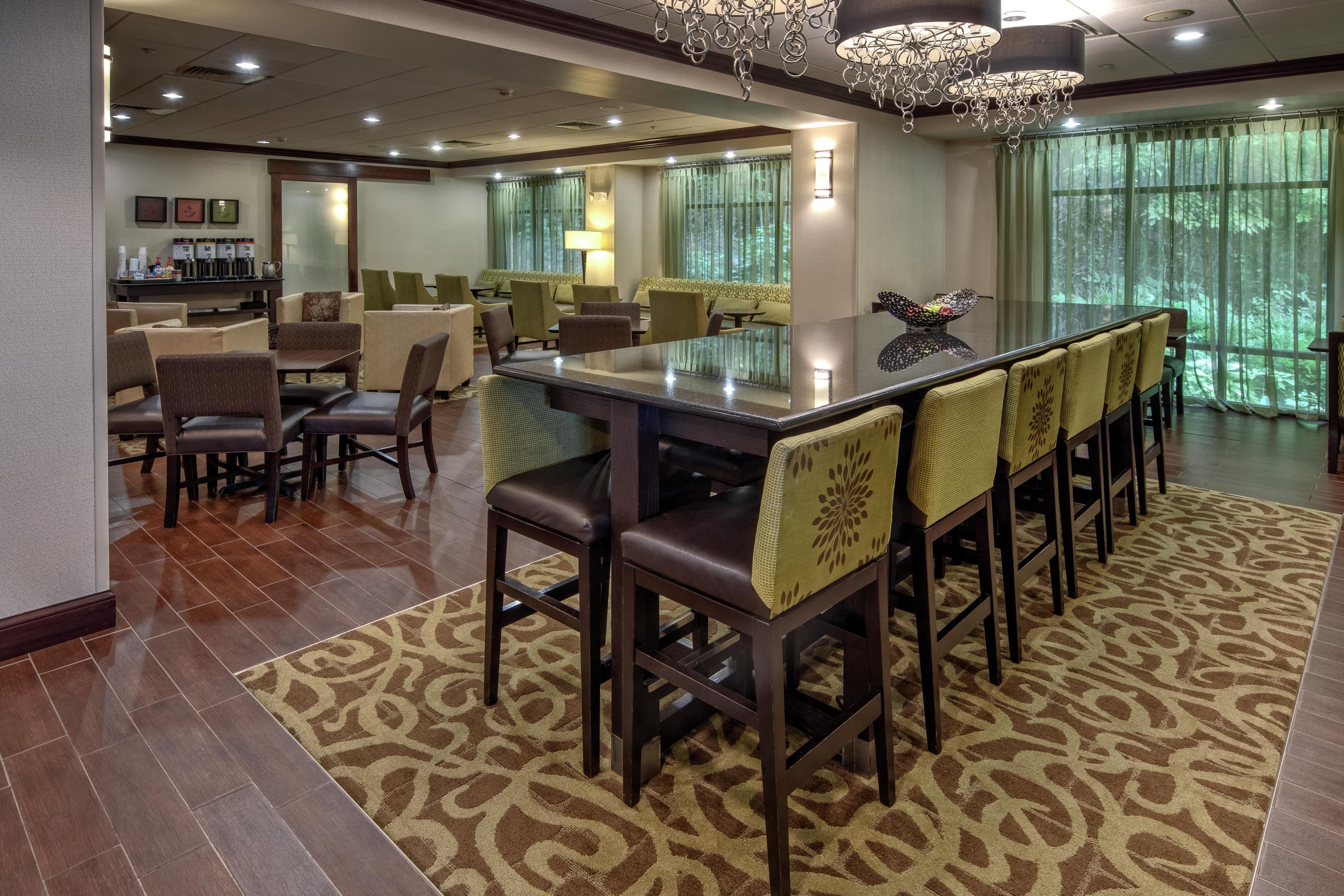 A hotel lobby with a bar area, seating arrangements, and a view of greenery outside.