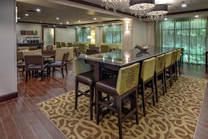 A hotel lobby with a bar area, seating arrangements, and a view of greenery outside. - Hampton Inn Cambridge (Cambridge)