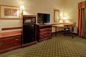 Habitación de hotel con kitchenette, televisor de pantalla plana, escritorio y silla, y alfombra estampada.