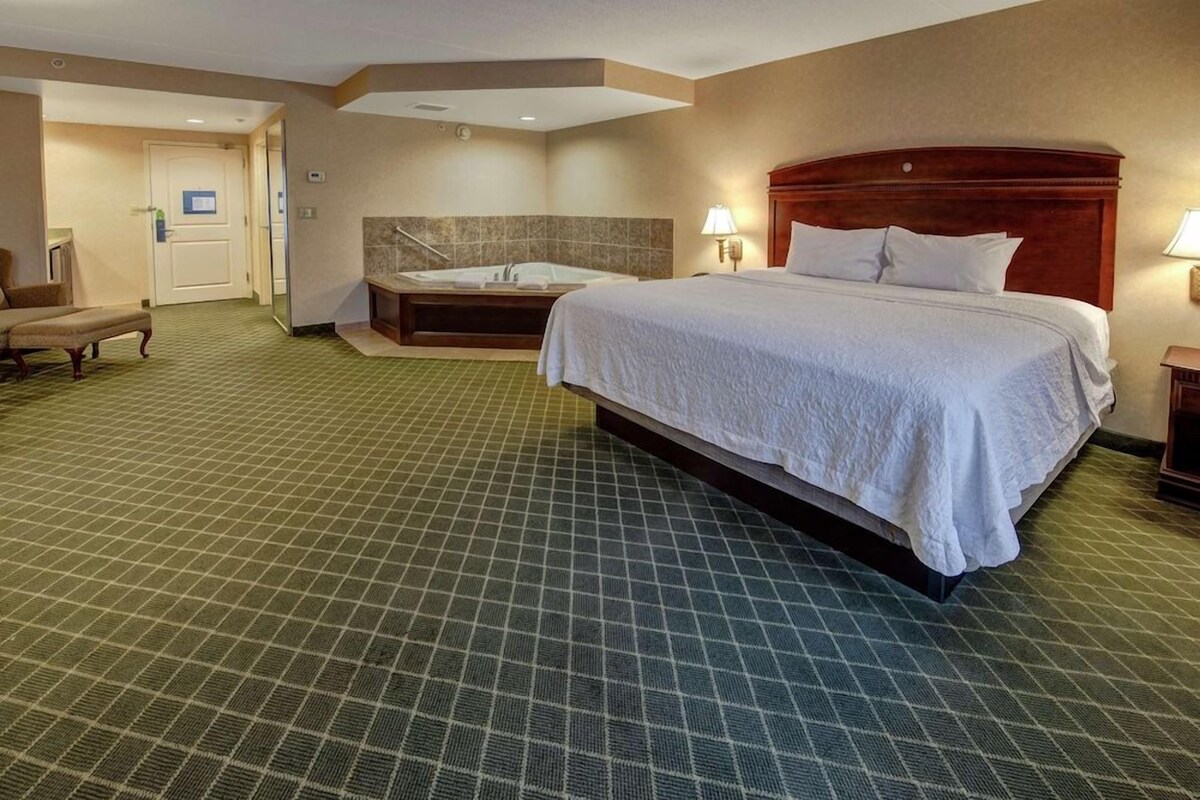 Habitación de hotel con una cama grande, una bañera independiente, una silla y una mesita.