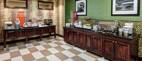 A hotel lobby with a checkered floor, a reception desk, and a buffet area with various food items and a coffee station.