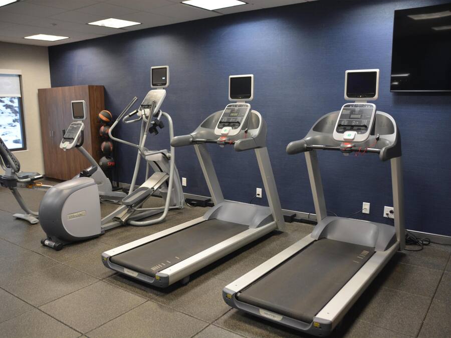 Three treadmills in a gym with a blue wall and a television mounted on the wall.