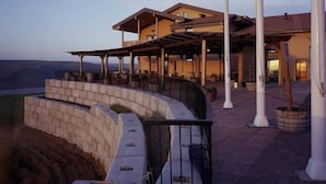 A two-story building with a covered patio area, a stone retaining wall, and a view of the landscape.