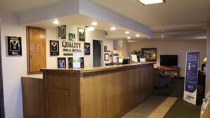 A reception area with a wooden reception desk, framed awards on the wall, and a sign for Quality Inn & Suites.