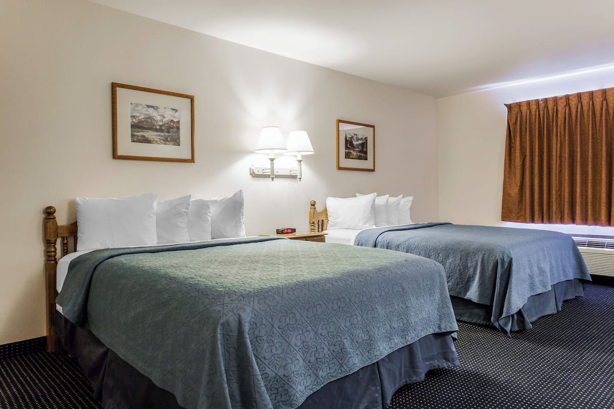 Quarto de hotel com duas camas, uma mesinha de cabeceira, um abajur e duas fotos emolduradas na parede.