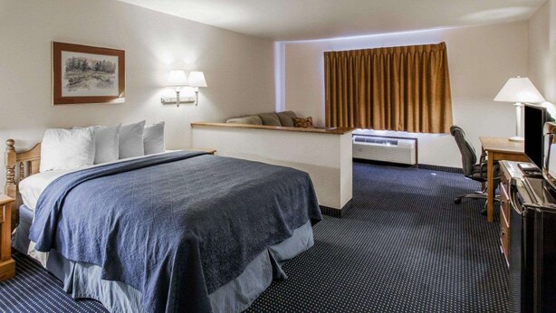A hotel room with a bed, bedside table, lamp, desk, chair, and a window with curtains.