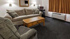 A hotel room with a sofa, a wooden coffee table, a television, a microwave, and a window with curtains.