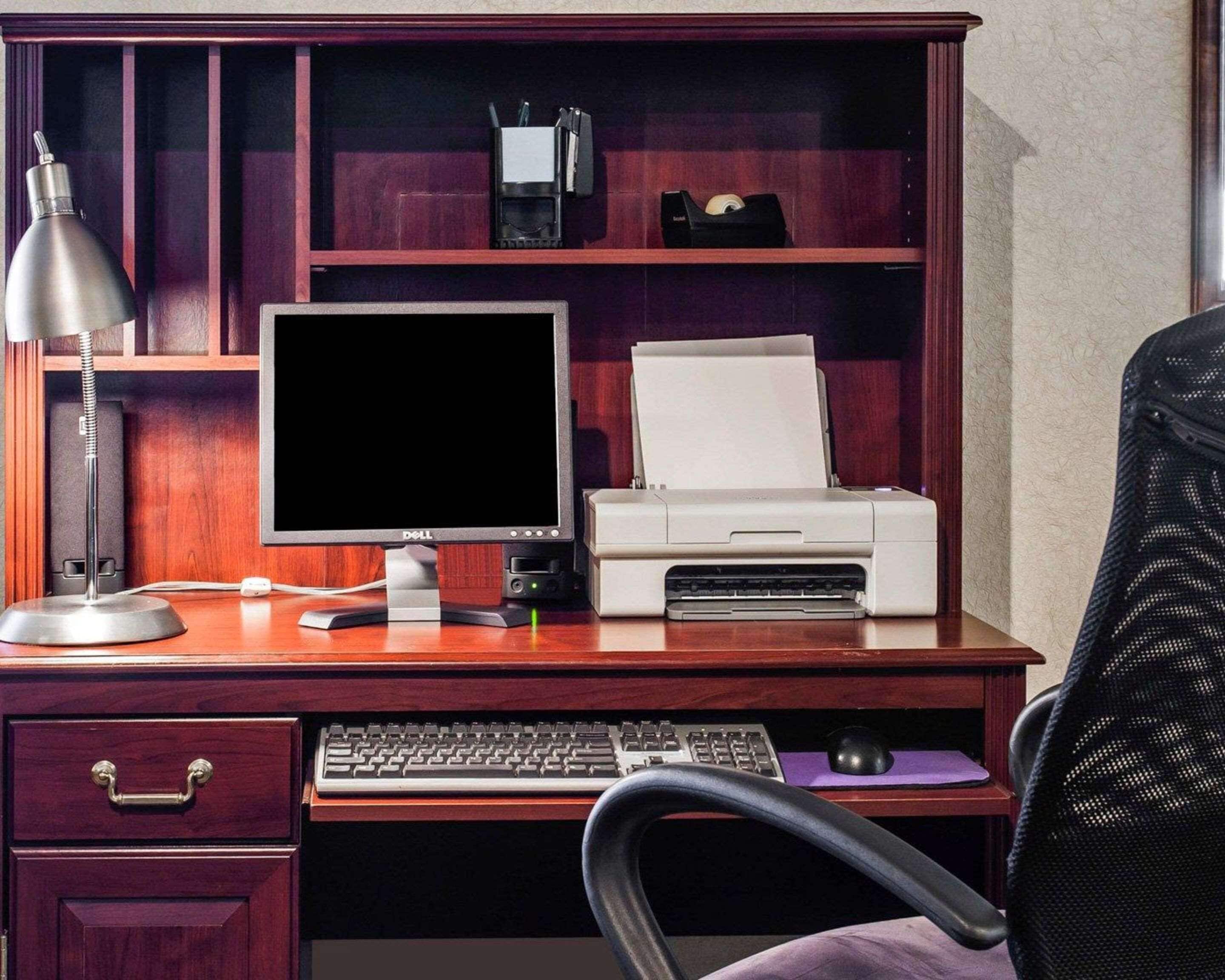 Een houten bureau met een computer, een printer, een lamp en een toetsenbord.