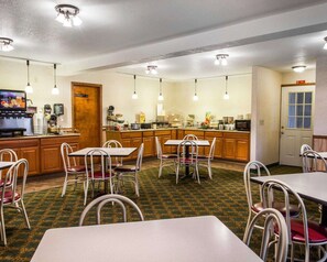 A hotel room with a kitchenette, dining area with tables and chairs, and a television displaying a menu.