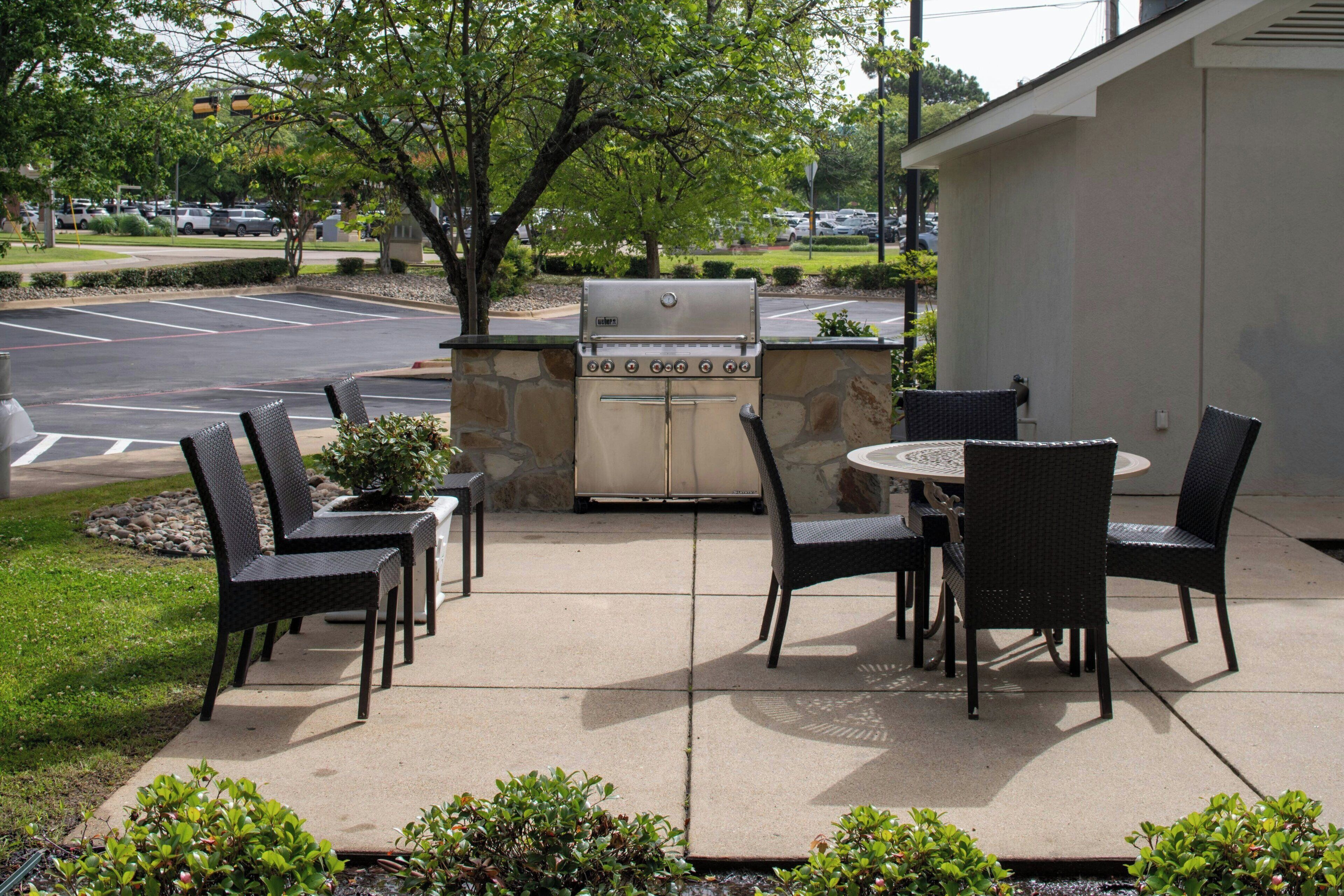 An outdoor patio with a grill, chairs, and a table.