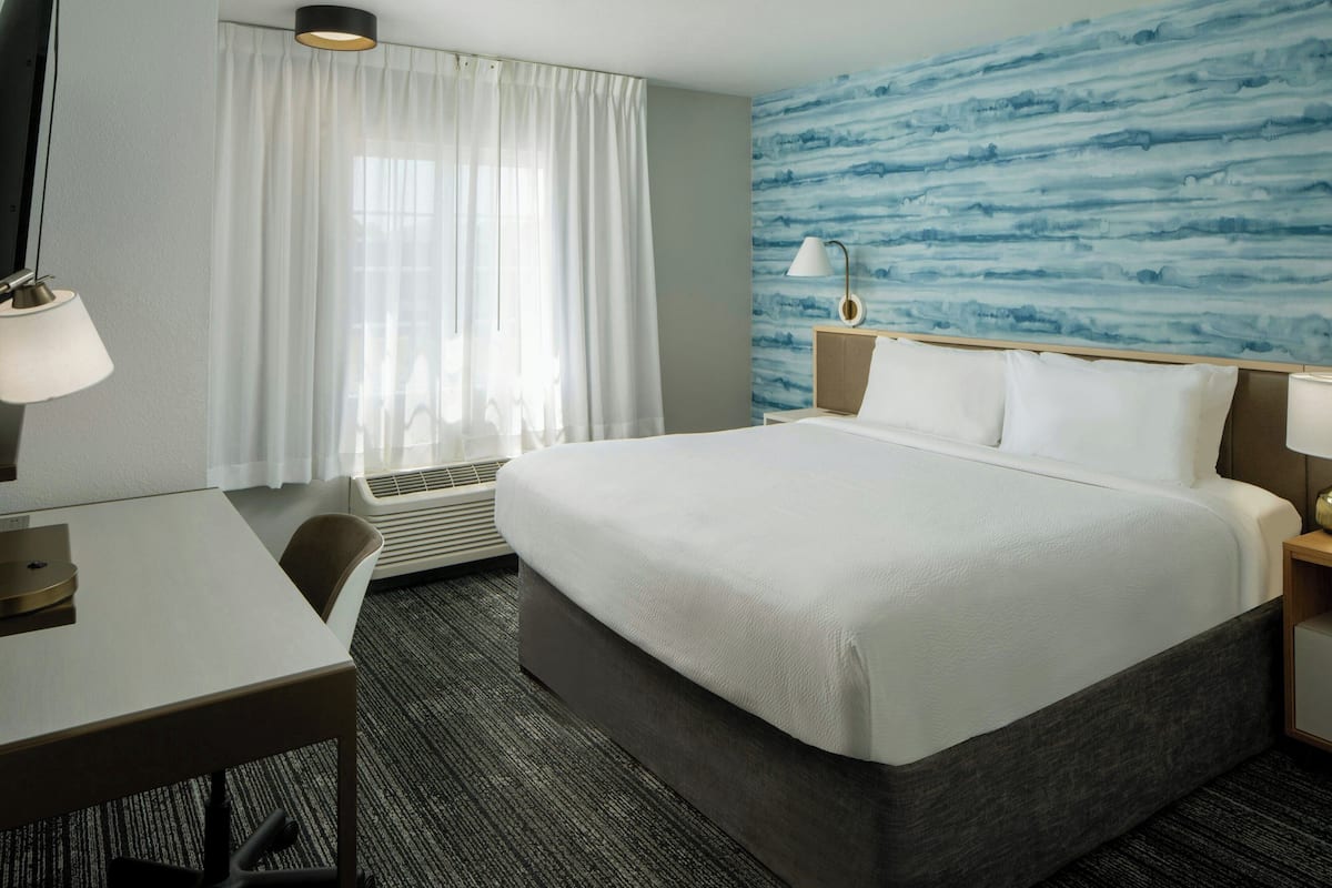 Une chambre d’hôtel avec un grand lit, un bureau, une chaise, une lampe et un mur orné d’un motif abstrait bleu.