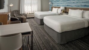 A hotel room with two beds, a desk, a chair, a TV, and a large window with curtains.
