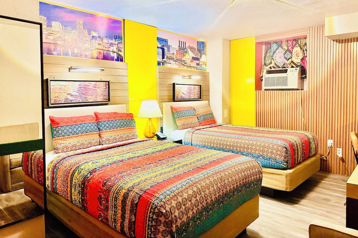 A hotel room with two beds, a cityscape mural on the wall, and a ceiling fan.