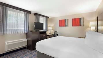 A hotel room with a large bed, a desk with a computer, a television, and two paintings on the wall.