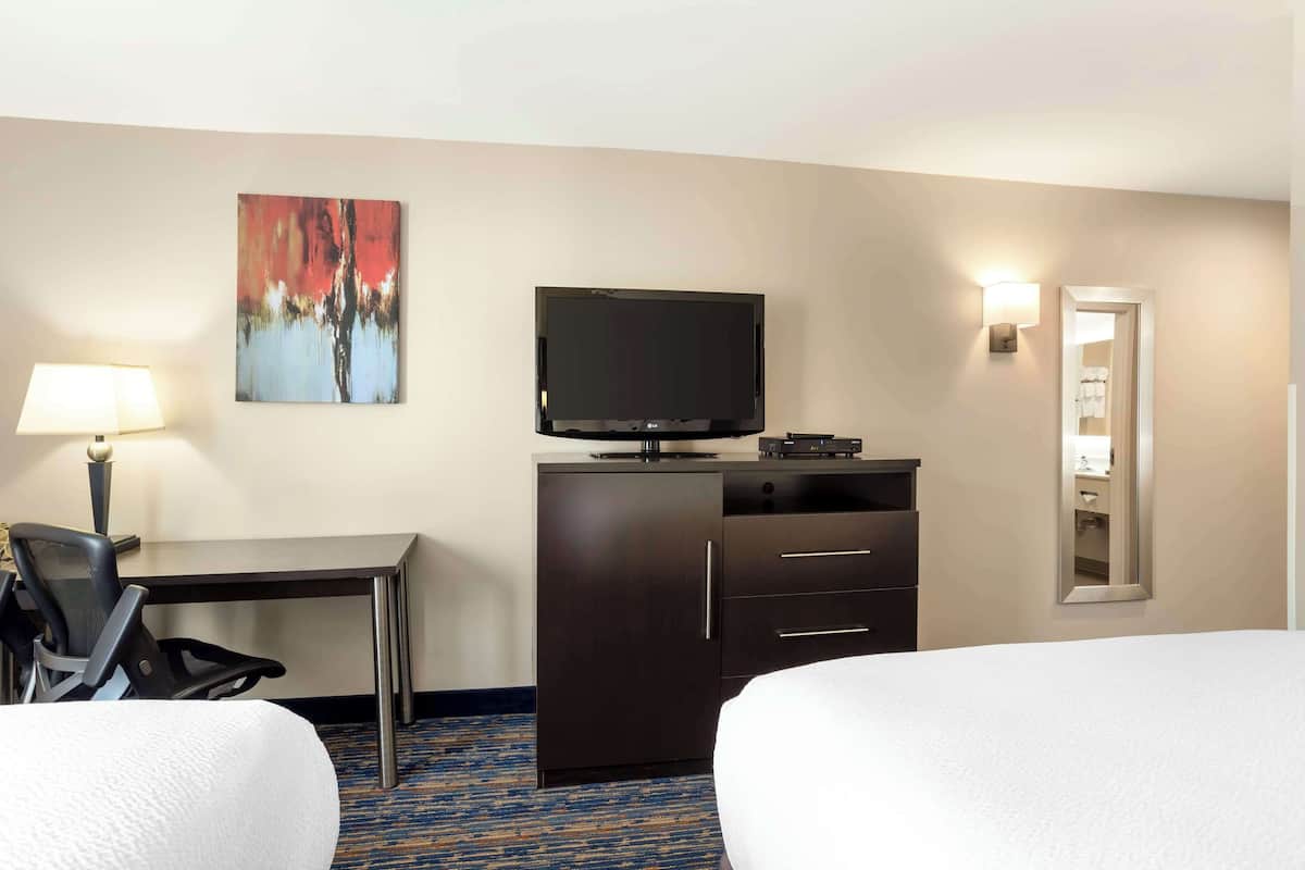 A hotel room with two beds, a desk with a chair, a television, a cabinet, and a painting on the wall.