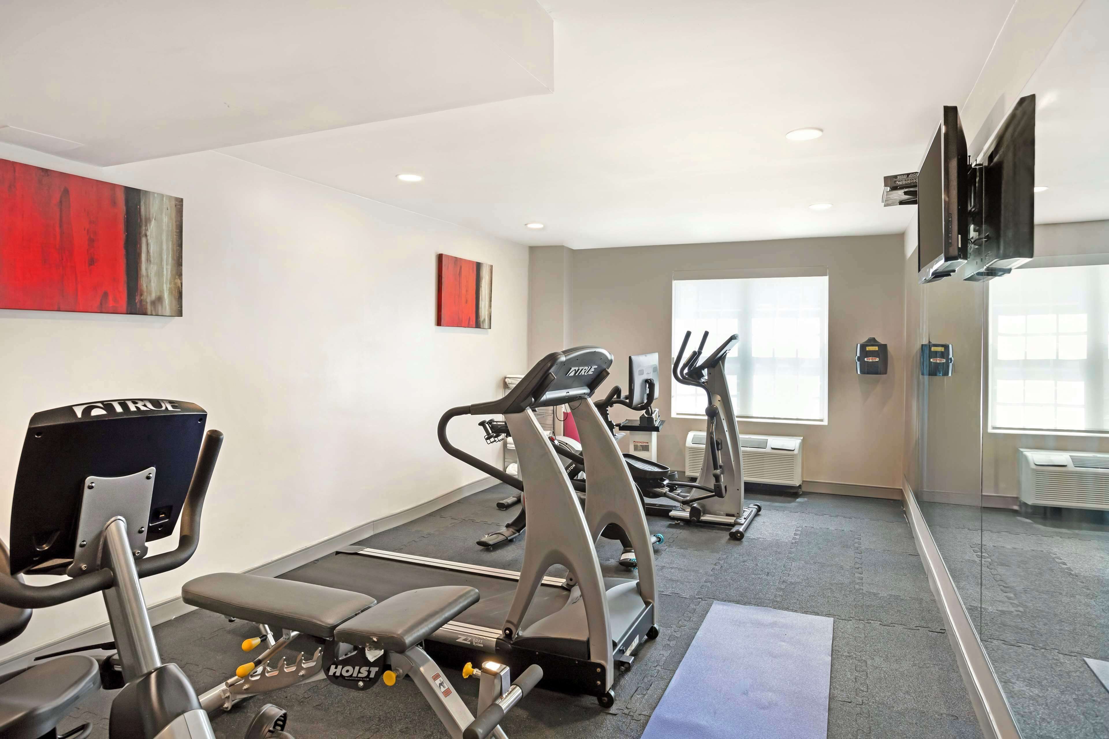A gym with treadmills, a stationary bike, and weight machines. There are large windows and a flat-screen TV mounted on the wall.