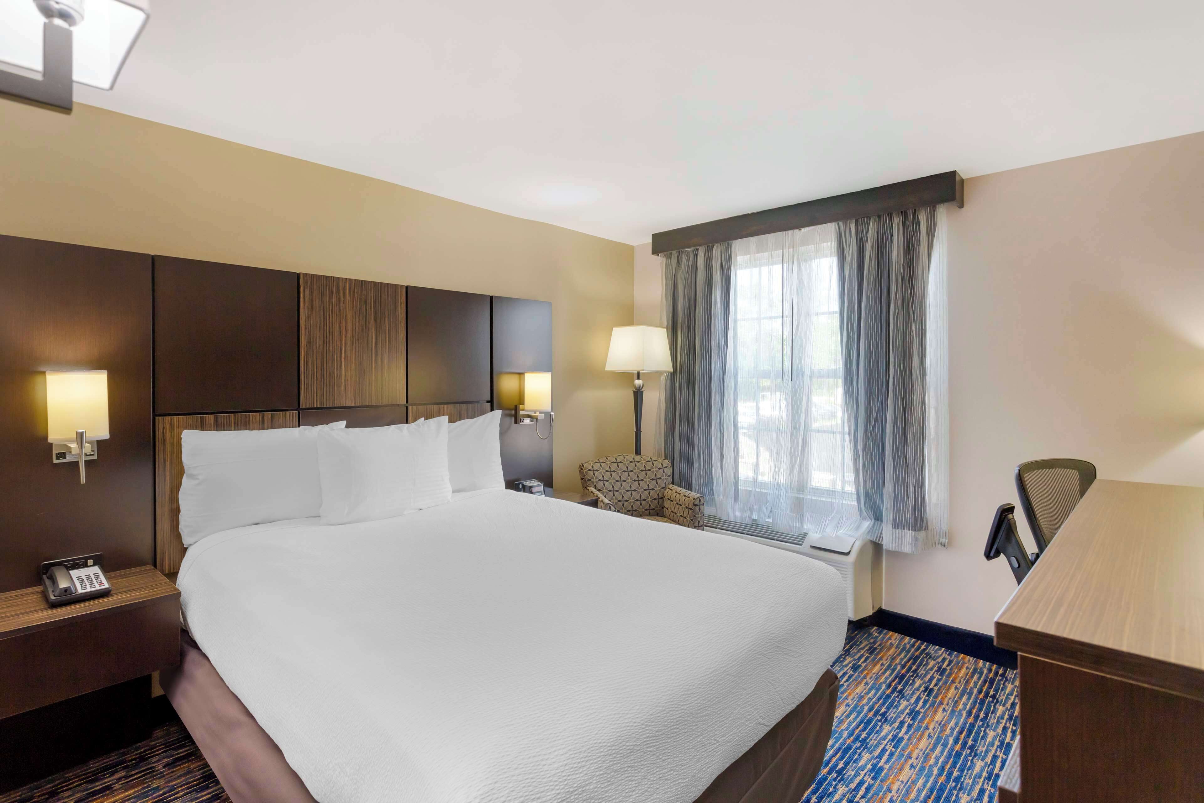 A hotel room with a large bed, bedside lamps, a desk, and a chair.