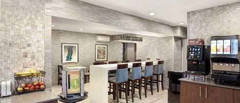 A modern kitchen with a bar area, equipped with a coffee machine and a fruit display.