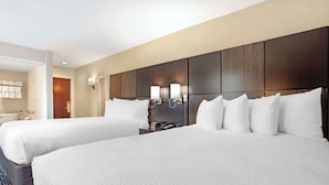A hotel room with two beds, a wooden headboard, wall-mounted lights, and a bathroom visible through an open door. - Best Western Plus Fairfield Hotel (Fairfield)