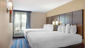 Habitació d'hotel amb dos llits, una finestra gran amb cortines, una làmpada penjada a la paret i un sòl amb moqueta.
