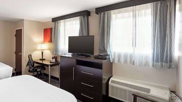 A hotel room with a bed, a desk with a chair, a television, and an air conditioning unit.