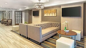 A modern hotel lobby with a large sofa, a round table, and a flat-screen TV mounted on the wall. - Best Western Plus Fairfield Hotel (Fairfield)