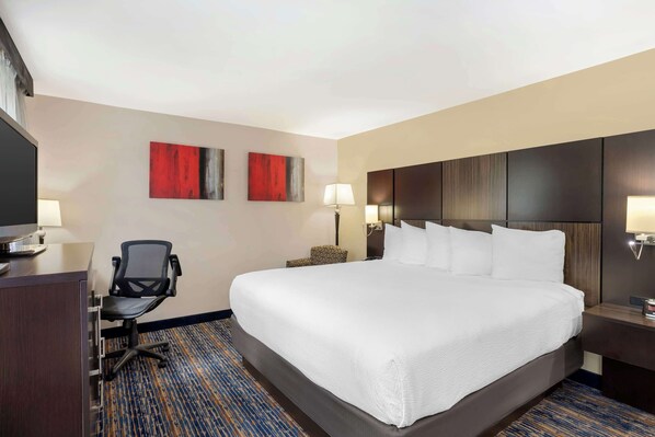 A hotel room with a large bed, a desk with a chair, a TV, and two paintings on the wall.