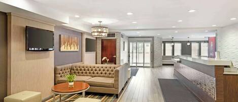 A modern hotel lobby with a sofa, a TV, a chandelier, and a reception desk.