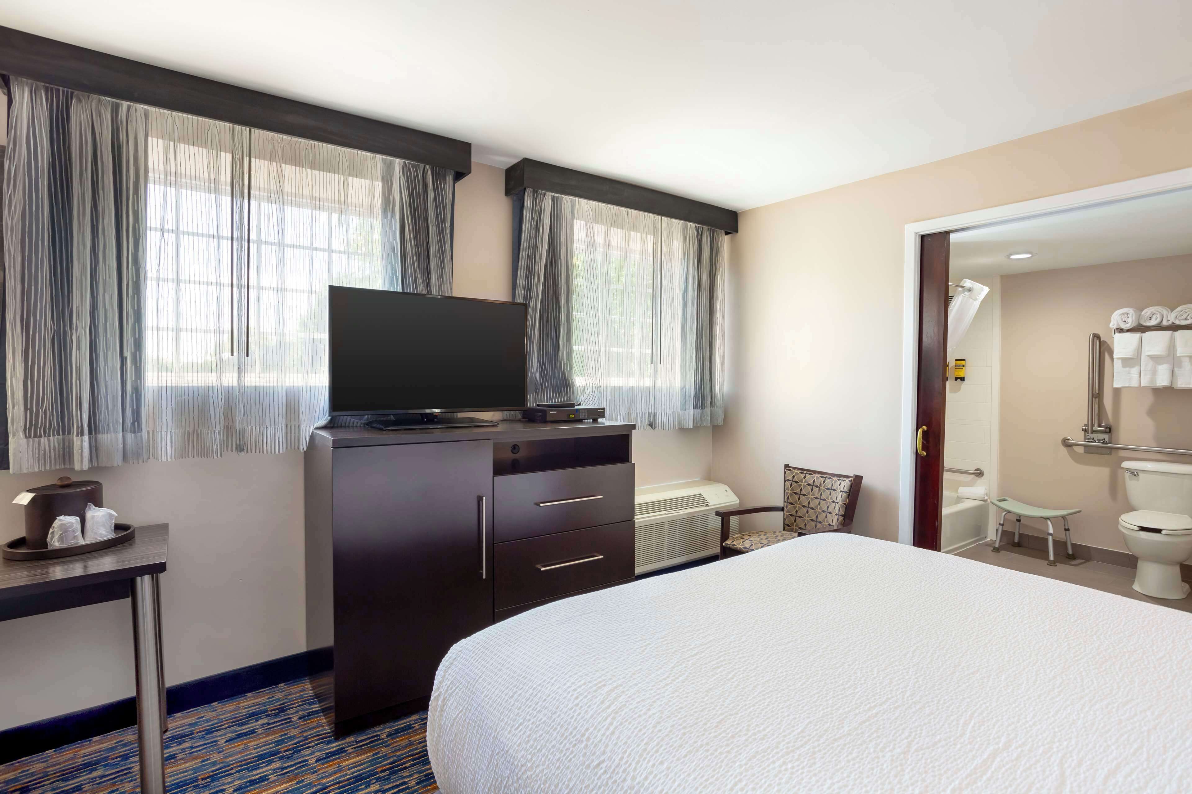 A hotel room with a bed, a TV on a dresser, a desk with a chair, and a bathroom visible through an open door.
