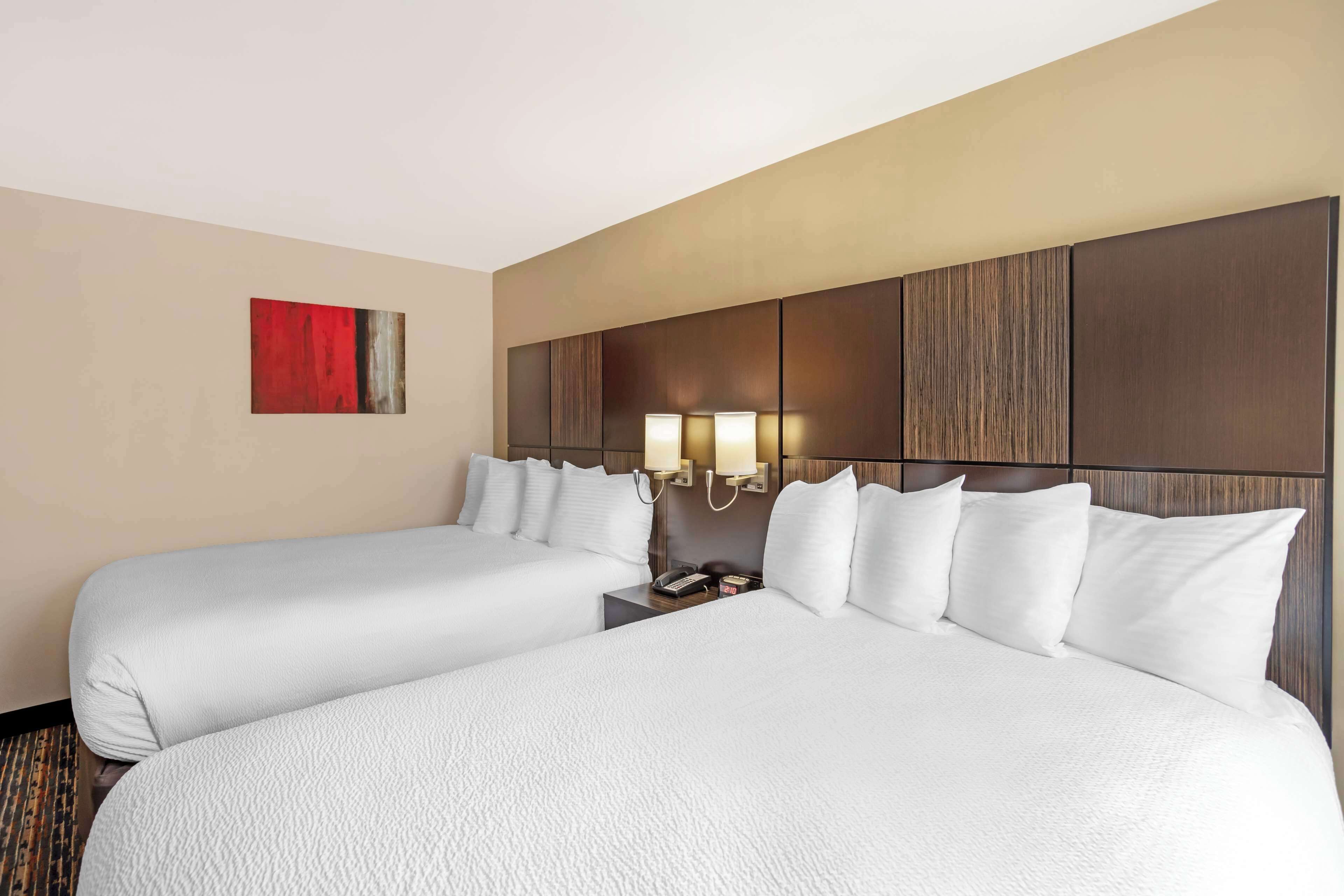 A hotel room with two beds, a red abstract painting on the wall, and a nightstand with a lamp.