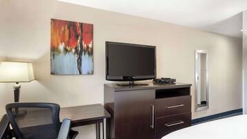 A hotel room with a bed, a desk with a chair, a television, a cabinet, and a painting on the wall.