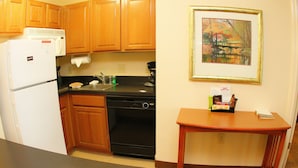 A compact kitchen with wooden cabinets, a black stove, a white refrigerator, and a small wooden table. - Staybridge Suites Houston Willowbrook by IHG (Houston)