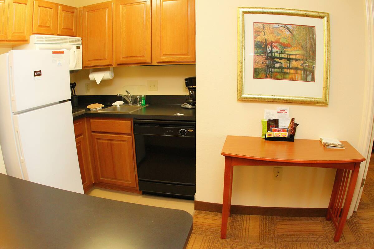 A compact kitchen with wooden cabinets, a black stove, a white refrigerator, and a small wooden table.