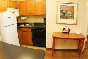 A compact kitchen with wooden cabinets, a black stove, a white refrigerator, and a small wooden table. - Staybridge Suites Houston Willowbrook by IHG (Houston)